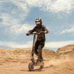 Riding the KuKirin G2 Ultra all-terrain electric scooter across a dusty desert trail.